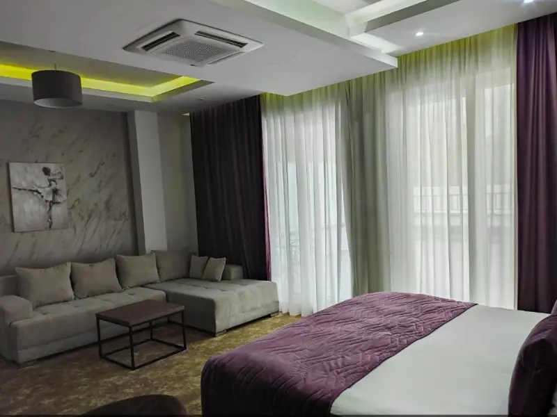 Apartman u Hotel Vrnjačke Terme sa bračnim krevetom sa ljubičastim prekrivačem, sivim ugaonim kaučom, mermernim zidovima, slikom balerine i zelenim LED osvetljenjem