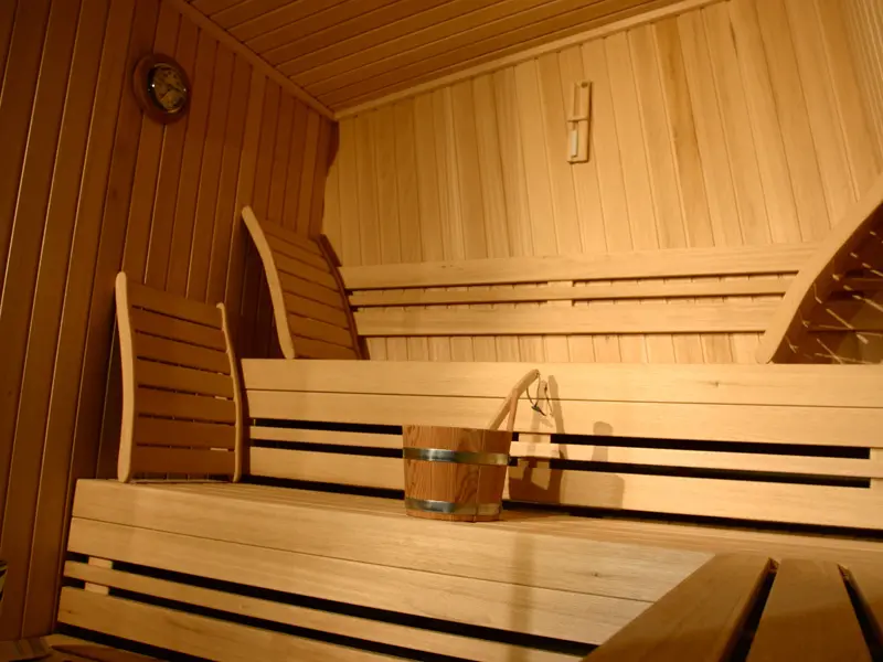 Finska sauna u Hotel Zira Beograd sa drvenim klupama od svetlog drveta, naslonima, drvenom kofom i satom na zidu