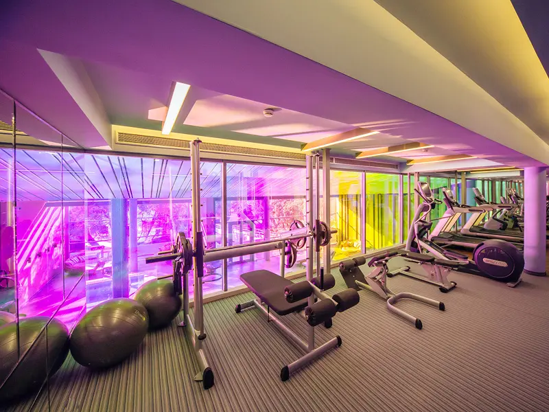 Fitnes centar u Maestral Resort & Casino sa ljubičastim ambijentalnim osvetljenjem, spravama za vežbanje, tegovima i pilates loptama