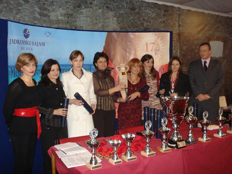 Svečana ceremonija dodele nagrada na Jadranski sajam Budva sa učesnicima, peharima na stolu i logom sajma u pozadini