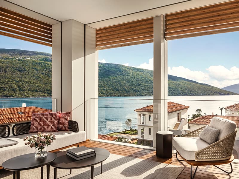 Dnevna soba apartmana u One & Only Portonovi sa modernim nameštajem, pletenom foteljom i panoramskim pogledom na more i planine