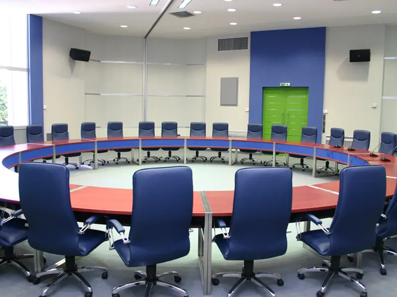 Konferencijska sala u ERA Group Skopje Fair Congress Center sa okruglim stolom, plavim kožnim foteljama, mikrofonima, plavim zidnim akcentima i zelenim vratima