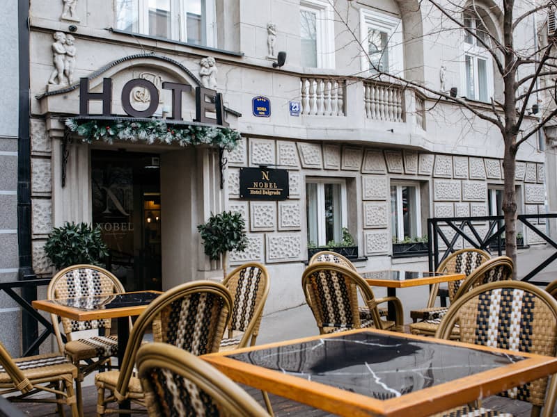 Eksterijer Hotel Nobel Gallery sa elegantnom fasadom, natpisom HOTEL, skulpturama na fasadi, ulazom sa žardinjerama i spoljnom terasom sa pletenim stolicama