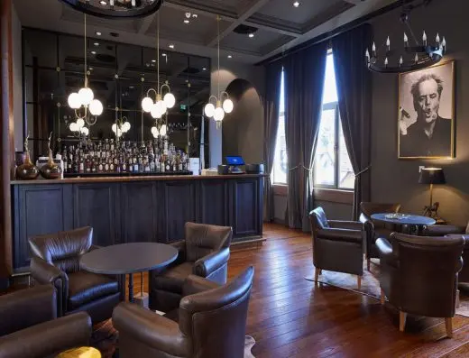 Bar u BOR Hotel by Karisma sa tamnim zidovima, kožnim foteljama, šankom, visećim lusterima sa kuglastim sijalicama i portretom na zidu