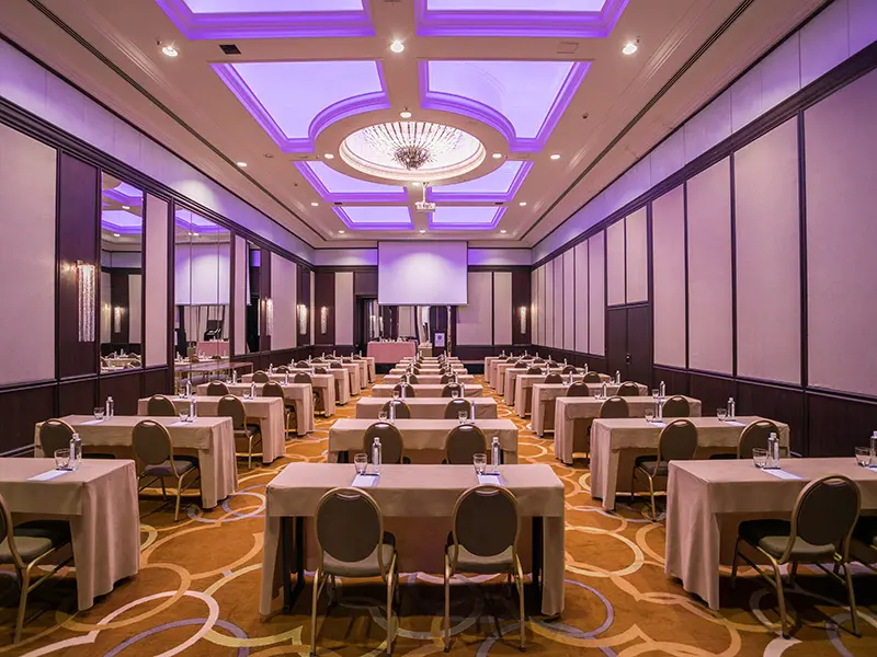 Balska dvorana u Hyatt Regency Beograd sa školskim rasporedom stolova, ljubičastom rasvetom, kristalnim lusterom i projektorskim platnom