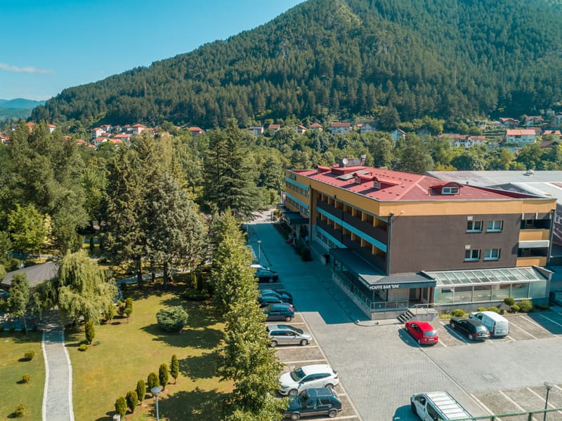 Aerial pogled na Garden City Hotel Konjic & Resort sa crvenim krovom, parkingom, zelenim travnjakom, drvoredima i planinom u pozadini