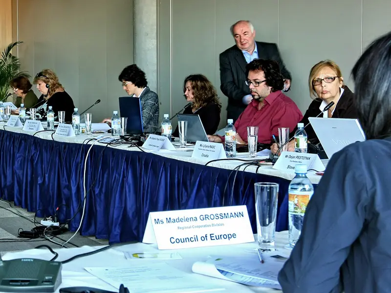 Konferencija u Hotel Zira Beograd sa delegatima za predsedničkim stolom, mikrofonima, laptopima, imenicama i plavim stolnjakom