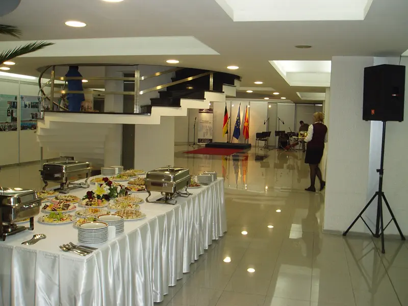 Foaje u ERA Group Skopje Fair Congress Center sa ketering bifeom, belim stolnjacima, zastavama, muzičarima, spiralnim stepeništem i zvučnicima