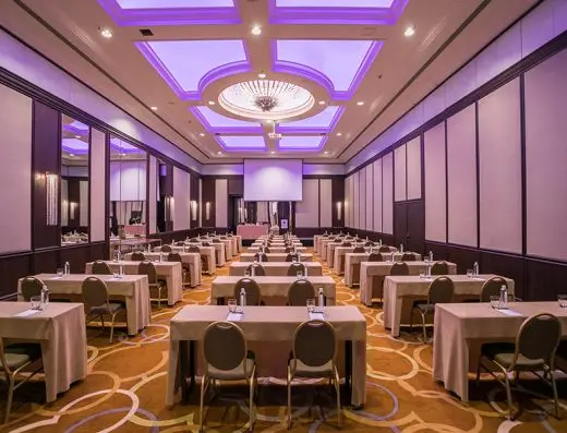 Balska dvorana u Hyatt Regency Beograd sa školskim rasporedom stolova, ljubičastom rasvetom, kristalnim lusterom i projektorskim platnom