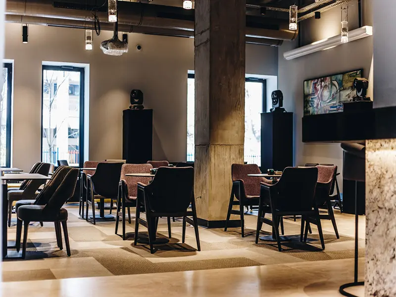 Bar i lounge zona u Hotel Mona Plaza sa crnim skulpturama na postoljima, slikom na zidu i stolicama u roze i braon tonovima