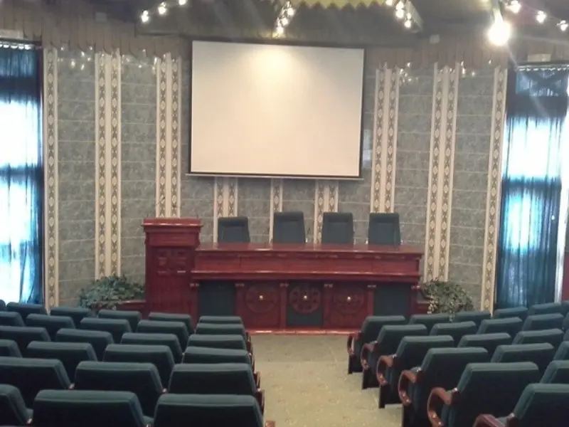 Konferencijska sala u Kongresnom centru Velika terasa sa tamnim foteljama, drvenom govornicom i projektorom