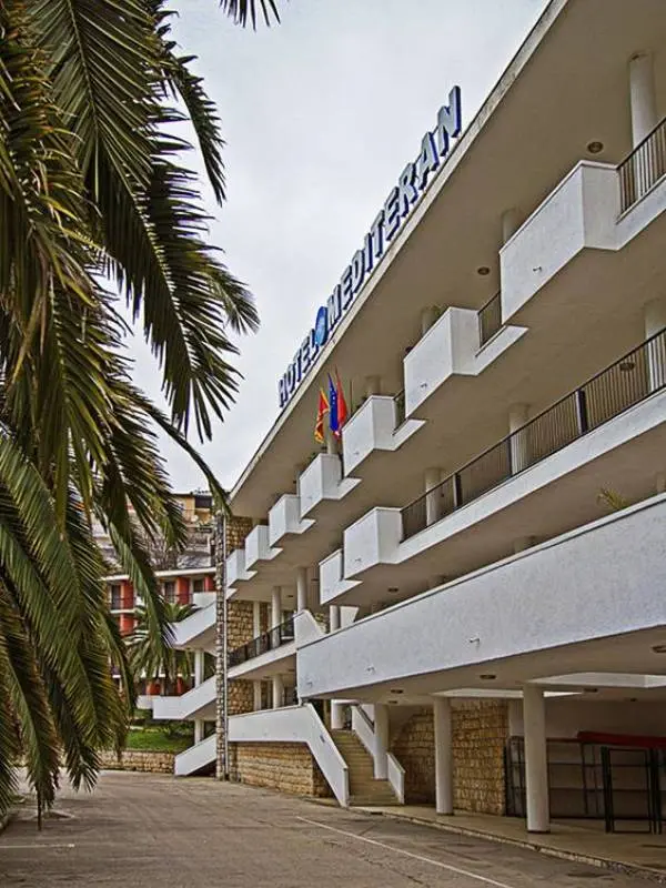 Bočni pogled na Hotel Mediteran Ulcinj sa belom fasadom, balkonima, natpisom, palmom i kamenim stepenicom