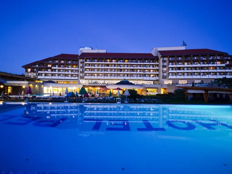 Noćni pogled na Hunguest Hotel Pelion Superior sa osvetljenom fasadom, spoljašnjim bazenom i odrazom u vodi
