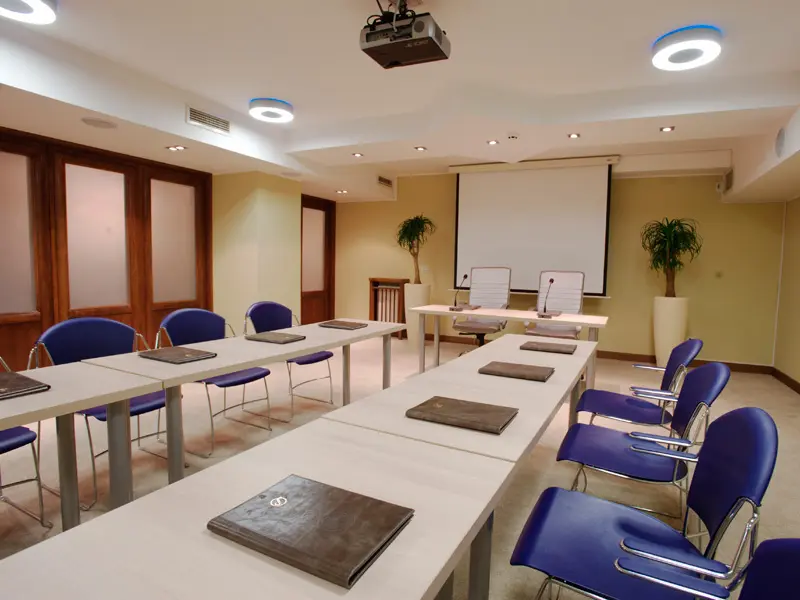 Konferencijska sala u Hotel Prestige Beograd sa stolovima u U-rasporedu, plavim stolicama, projektorom na plafonu i brendiranim fasciklama