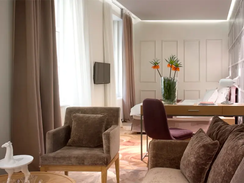 Apartman u Jump Inn Hotel Belgrade sa braon plišanim foteljama, radnim stolom, narandžastim cvećem, bež zavesama i dekorativnim zidnim panelima