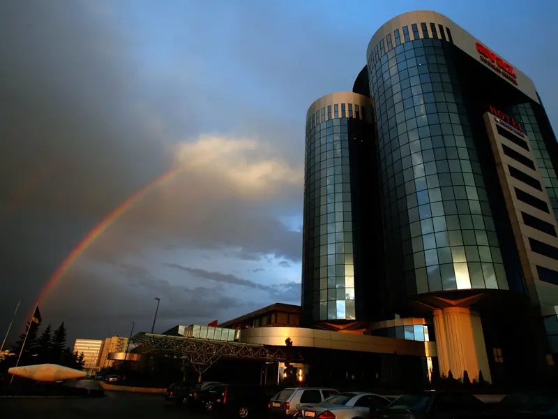 Fasada Radon Plaza Hotel noću sa staklenim kulama, dugom na nebu, dramatičnim oblacima i osvetljenim ulazom