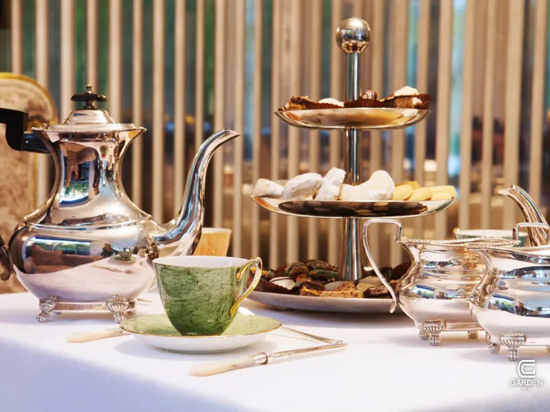 Detalj serviranja u Garden Spa Boutique Hotel sa srebrnim čajnikom, zelenom šoljicom, trostrukom etažerom sa kolačima i elegantnim priborom