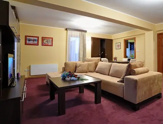 Dnevni boravak apartmana u Solaris Resort sa ugaonim kaučem, TV-om, bordo tepihom i uramljenim slikama