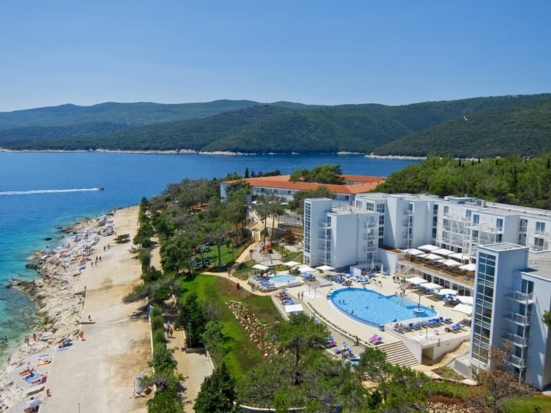 Aerial pogled na Valamar Sanfior Hotel sa belom zgradom, spoljnim bazenom, plažom sa kupačima, borovima i tirkiznim morem