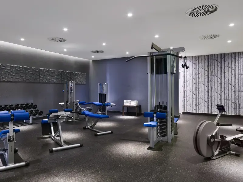 Fitnes centar u Hotel Park Plaza Histria Pula sa plavim spravama za vežbanje, tegovima, tamnim zidovima i modernim enterijerom