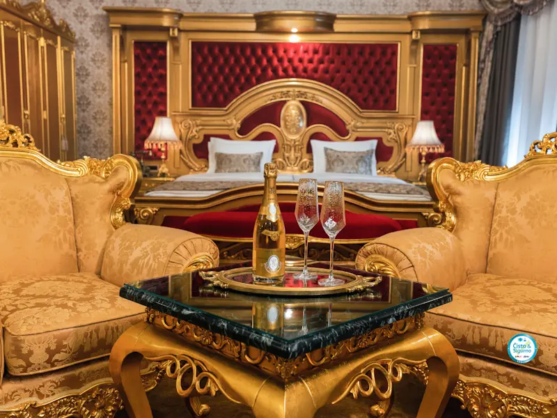 Apartman u Prezident Palace Belgrade sa zlatnim baroknim kaučem, šampanjcem na stočiću, crvenim uzglavljem kreveta i kristalnim lusterom u pozadini