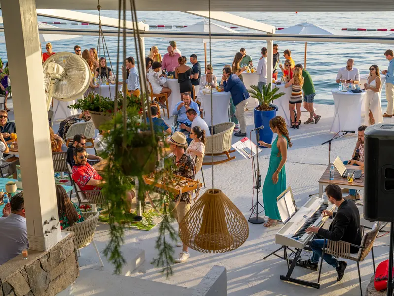 DogaÄ‘aj na plaÅ¾i u Key West Beach & Restaurant sa Å¾ivom muzikom, kokteil stolovima i gostima uz more