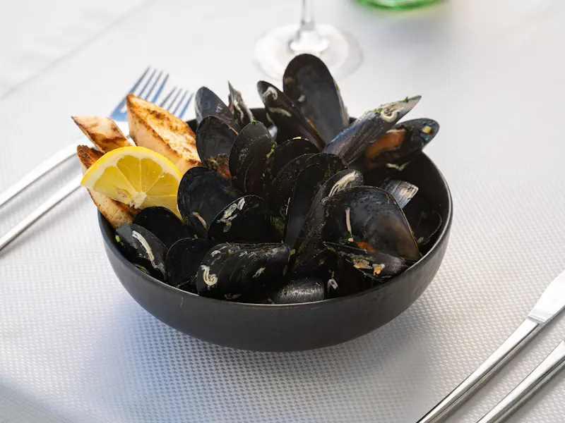 Dagnje u crnoj činiji sa limunom i tostiranim hlebom u Dukley Seafront Restaurant and Beach na belom stolnjaku