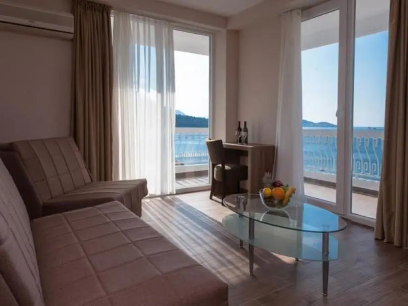 Dnevna soba apartmana u Sato Hotel Conference & Spa Resort hotelu sa bež kaučem, staklenim stolom, voćem i panoramskim pogledom na more