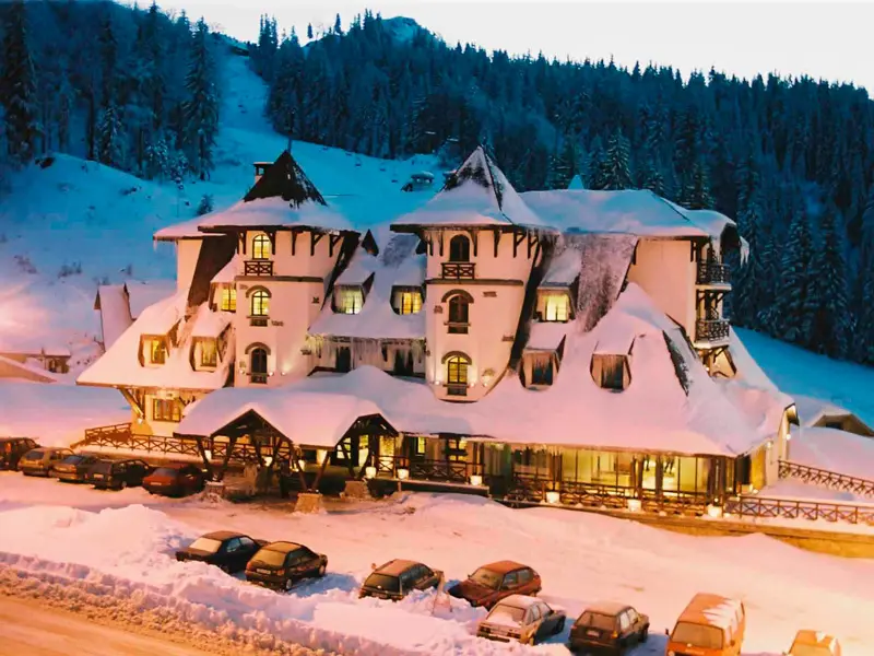 Noćni pogled na Termag Hotel Jahorina sa snežnim krovovima, kulama, toplim osvetljenjem iz prozora, parkingom i šumom u pozadini