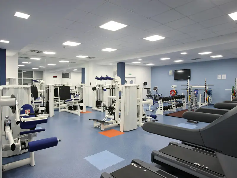 Fitnes sala u Hotel Srbija Lux sa spravama za snagu, bučicama, olimpijskom šipkom, TV ekranom i plavim podom