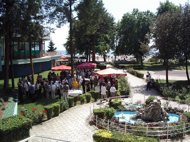 Bašta Hotel Drim sa koktel prijemom, kamenom fontanom, zelenim travnjakom, visokim borovima i pogledom na jezero