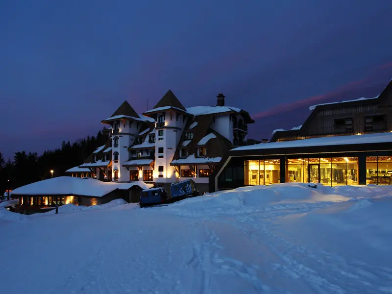 Panoramski pogled na Termag Hotel Jahorina u sumraku sa snežnim pejzažom, osvetljenim prozorima, kulama i borovima u pozadini