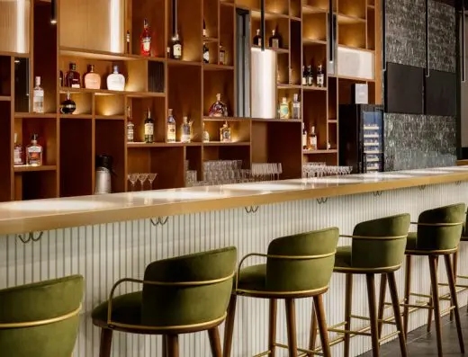 Bar u Pullman Zagreb sa zelenim plišanim barskim stolicama, belim šankom, drvenim policama sa pićima i toplim ambijentalnim osvetljenjem