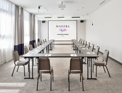 Mala konferencijska sala u Hotel International Zagreb sa stolovima u U-rasporedu, projektorskim platnom i sivim stolicama