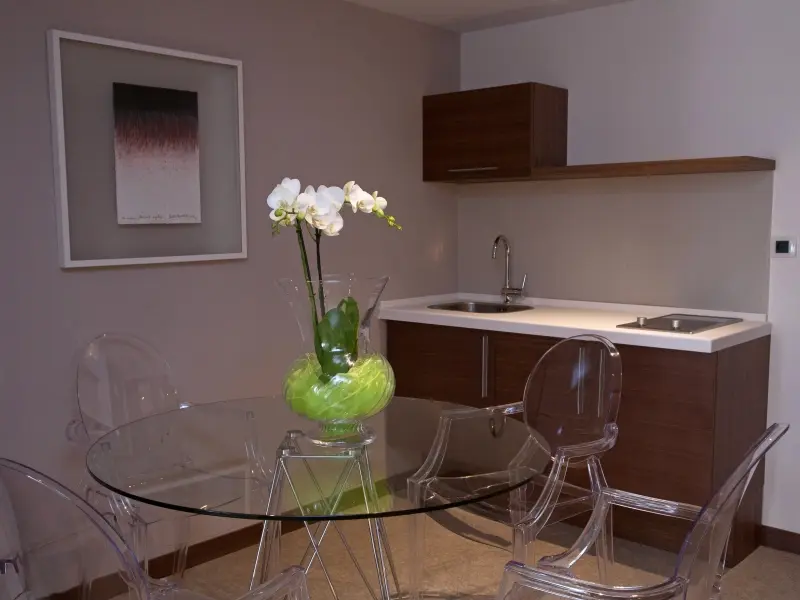 Apartman u Hotel Aurel sa mini kuhinjom, staklenim trpezarijskim stolom, prozirnim stolicama i belom orhidejom