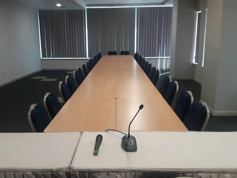 Konferencijska sala u Tre Canne hotelu sa dugačkim stolom, plavim stolicama, mikrofonom i vertikalnim roletama