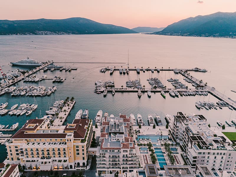 Aerial pogled na Regent Porto Montenegro i marinu u zalazak sunca sa žutom fasadom hotela, bazenima, jahtama i Bokokokotorskim zalivom