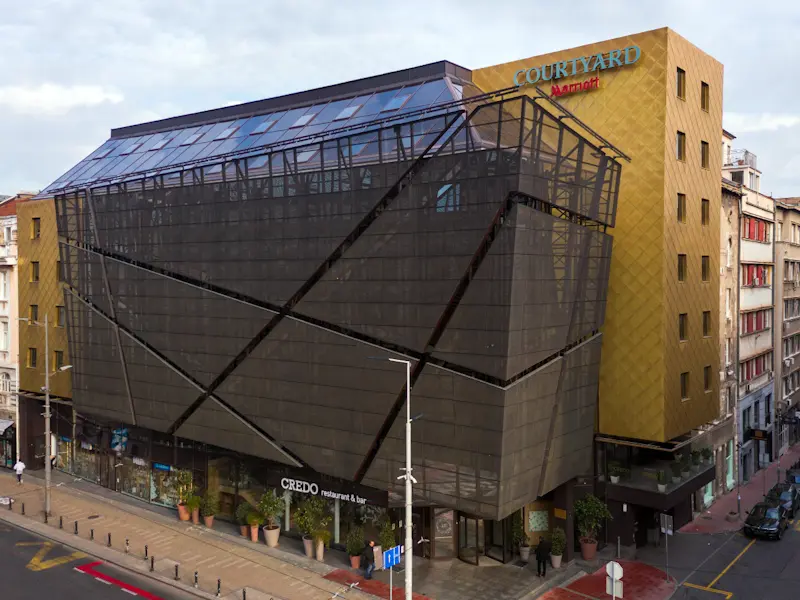 Eksterijer hotela Courtyard Belgrade City Center sa modernom ugaonom tamnom fasadom, žutim akcentima i pogledom na gradsku ulicu