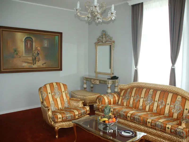 Dnevna soba apartmana u Zepter Hotel Vrnjačka Banja sa klasičnim nameštajem u zlatnom okviru, prugastom tapaciranom garniturom, umetničkom slikom i kristalnim lusterom
