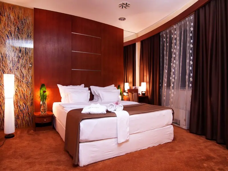 Suite soba u Radon Plaza Hotel sa bračnim krevetom, tamnim drvenim panelima, braon zavesama, uroljanim peškirima i apstraktnom slikom