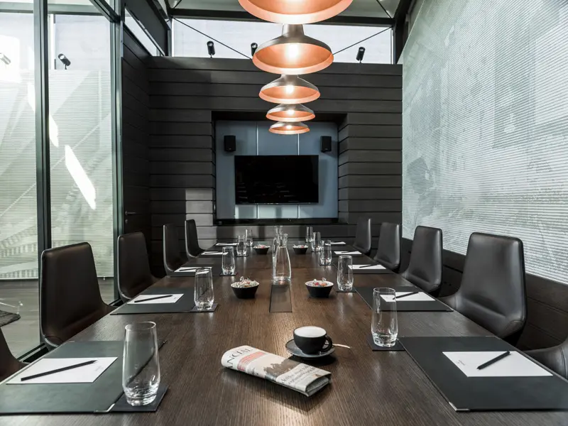 Boardroom sala u hotelu Radisson Collection Hotel Old Mill Belgrade sa tamnim drvenim stolom, crnim kožnim stolicama, bakarnim visećim lampama i televizorom na crnom zidu