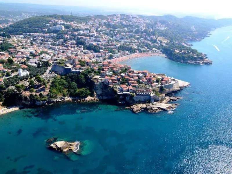 Aerial pogled na Ulcinj sa Starim gradom na poluostrvu, tvrđavom, plažom sa suncobranima, tirkiznim morem i panoramom grada