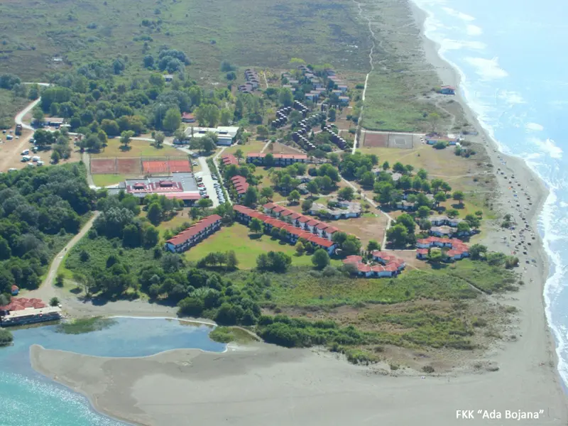 Aerial pogled na FKK naselje Ada Bojana u okviru HTP Ulcinjska rivijera sa bungalovima, crvenim krovovima, plažom, morem i zelenilom