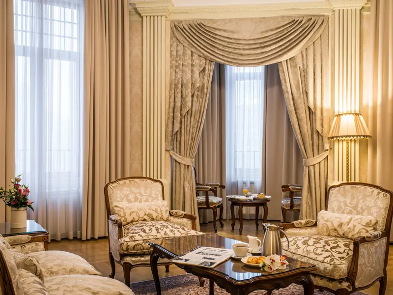 Salon apartmana u Hotel Moskva sa visokim zavesama, klasičnim foteljama, stonom lampom i doručkom na stočiću