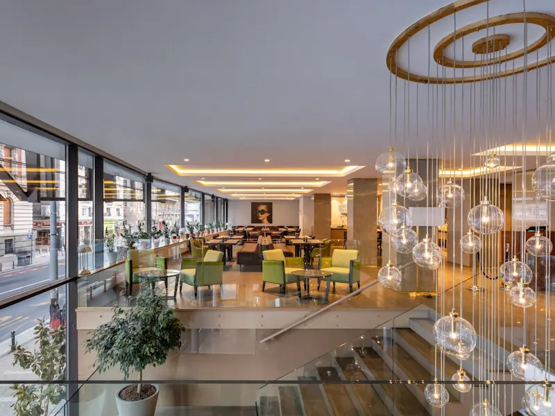 Restoran na gornjem spratu hotela Courtyard Belgrade City Center sa zelenim stolicama, staklenim kugla lusterima, panoramskim prozorima i pogledom na grad