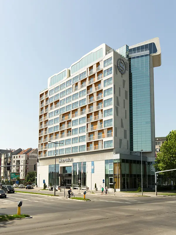 Eksterijer Hotel Sheraton Novi Sad sa modernom fasadom u bež i staklenoj boji, Sheraton logom, višespratnom strukturom i gradskim okruženjem