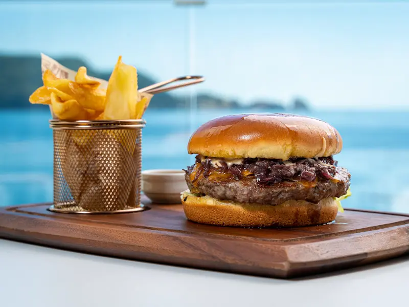 Burger sa karamelizovanim lukom i pomfritom na drvenoj dasci u Dukley Seafront Restaurant and Beach sa pogledom na more