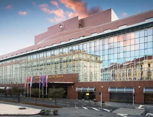 Spoljna fasada Sheraton Zagreb Hotela sa staklenom fasadom, zastavama i odrazom zgrada u sumrak