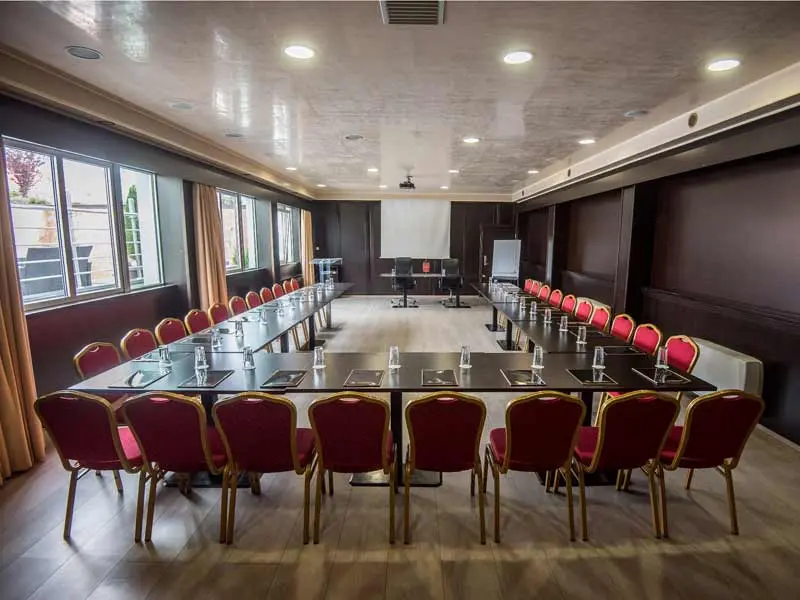 Konferencijska sala u Prezident Hotel sa U rasporedom, crvenim stolicama, tamnim stolovima i projektorom