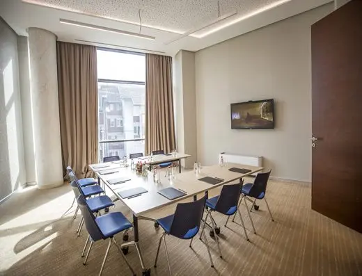Sala za sastanke u Hotel Tonanti sa stolom u U-rasporedu, plavim stolicama, TV ekranom i velikim prozorom sa zavesama